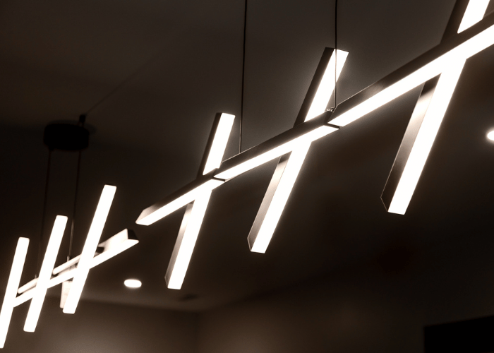Close-up of a modern, geometric LED pendant light fixture with angled bars suspended from the ceiling, providing ambient lighting in a contemporary interior space.