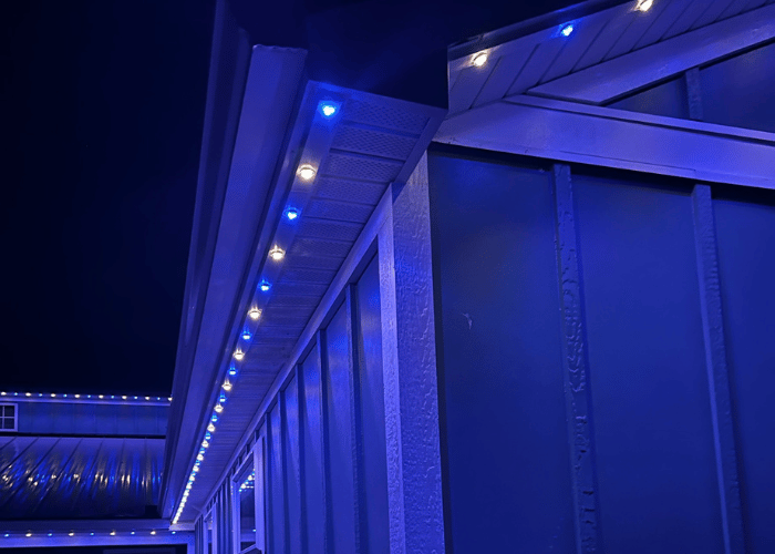 Close-up of Gemstone Lights installed along the soffit of a home, displaying alternating blue and white LED lights for permanent architectural and seasonal lighting.