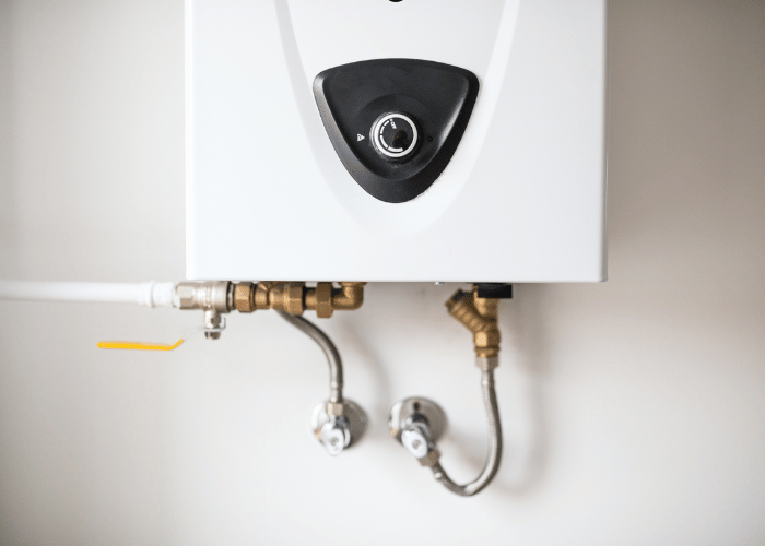 Close-up of a modern tankless water heater mounted on a wall, with visible plumbing connections for hot and cold water supply.