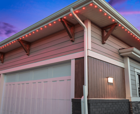 Close-up of a garage with red Gemstone Lights installed along the soffit, highlighting the modern exterior with wood accents and evening sky in the background.