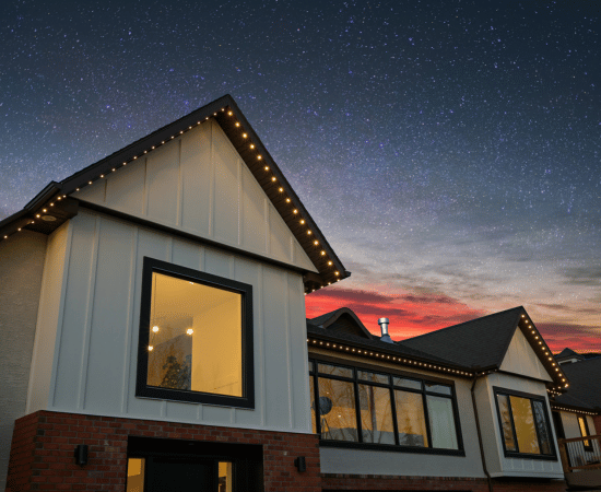 Modern home with black trim and white siding outlined by Gemstone Lights in a soft warm white, glowing against a sunset and star-filled sky.