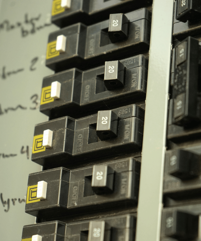 Close-up of a labeled electrical breaker panel with multiple 20-amp circuit breakers and handwritten circuit descriptions on the side.