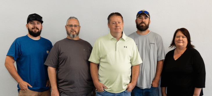 **Alt text:** Group photo of five C-U Trade Services team members standing against a plain white wall, including four men and one woman.