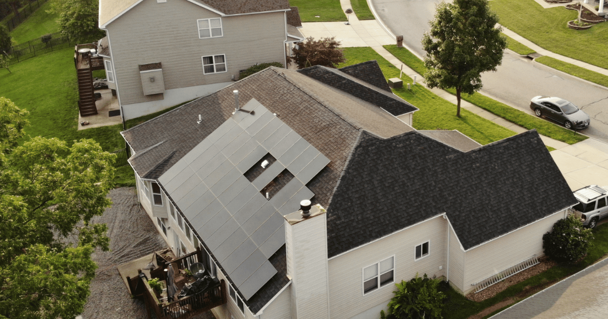 Aerial view of a suburban Central Illinois home with solar panels installed on the roof, surrounded by green lawns and a quiet residential street.