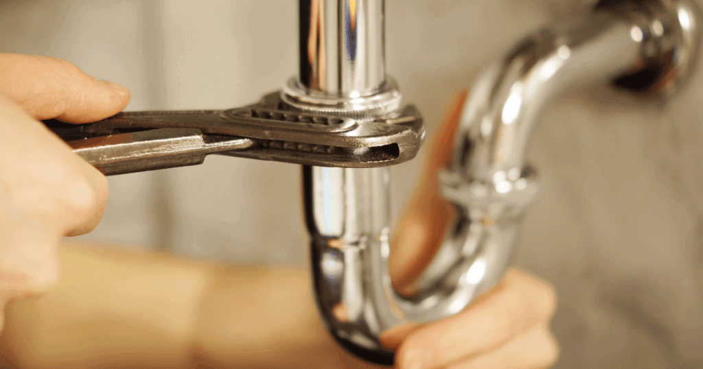 Plumber using a wrench to tighten a chrome P-trap drain pipe under a sink