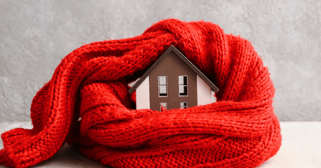 House wrapped in a red knit blanket, symbolizing efficient home heating and energy savings during cold weather.
