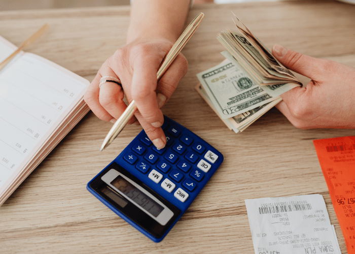 Hands counting cash and using a calculator next to receipts to budget for home maintenance costs
