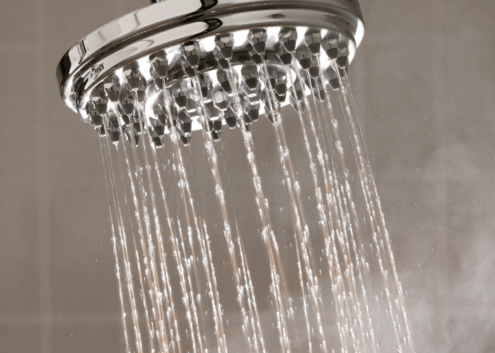 Chrome rain showerhead spraying water with steam rising, showing hot water reaching the shower faster
